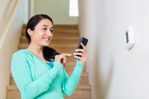 woman-on-smart-phone-standing-in-front-of-thermostat