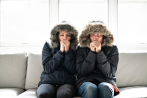 couple-sitting-on-couch-with-parkas-and-hoods-on