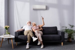 senior-couple-sitting-on-couch-with-mini-split-on-wall-behind-them