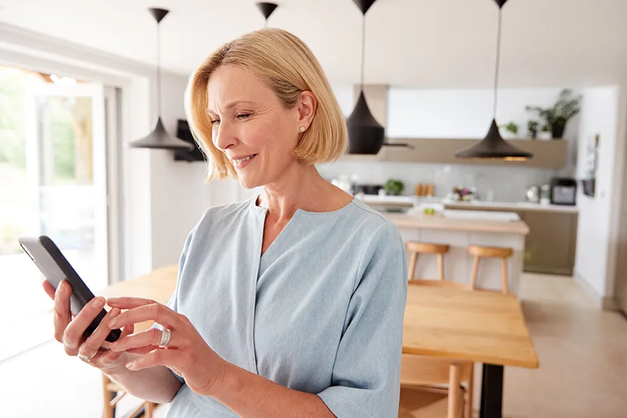 A middle-aged lady on her smartphone calling for Myers Heating + Air service in her modern home.