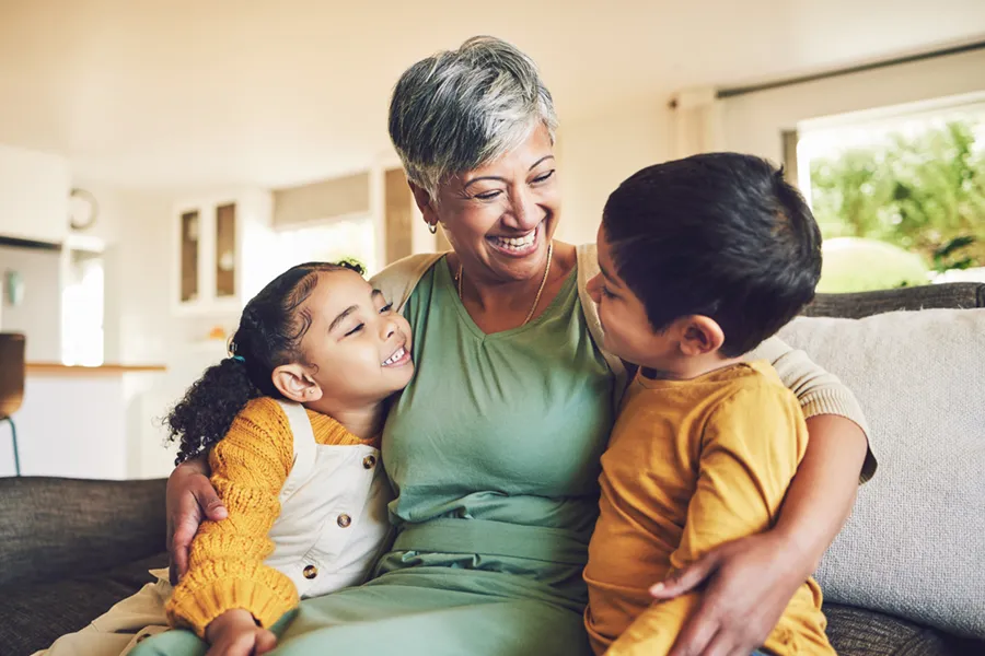 Grandmother smiling and holding her two grandchildren on a couch in a climate controlled home.