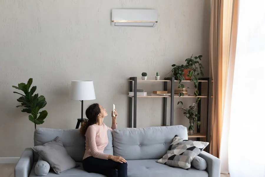 A young woman adjusting the temperature on her ductless mini-split with a remote in her living room.