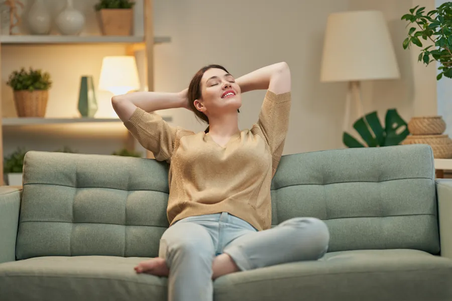 A young, Asian-American woman resting on the couch in her living room, breathing deep and enjoying the fresh air quality.