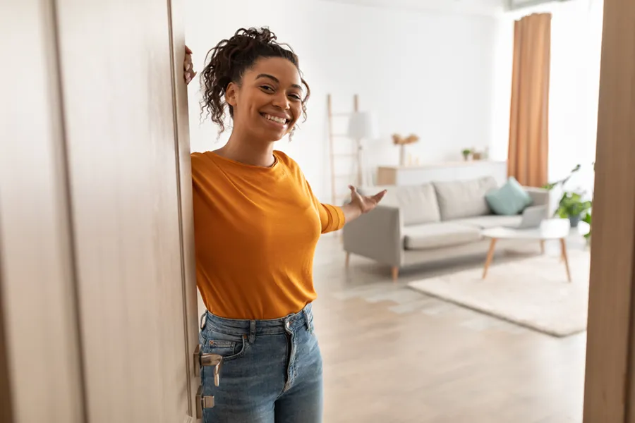 A young woman standing at the door to her home, inviting you in.