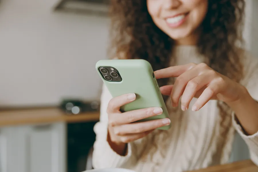 A young woman using her smartphone, tapping the screen and smiling.