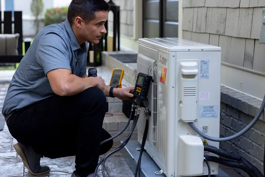 A Mitsubishi Diamond-certified HVAC technician installing a condenser unit outside a home.