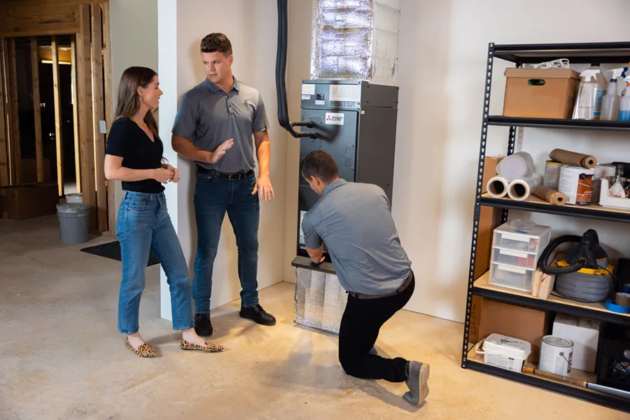 Mitsubishi HVAC technicians installing a new furnace in a young woman's home, showing her how to operate it.
