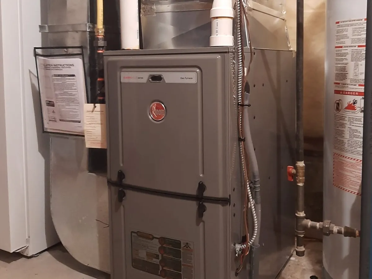 Modern high-efficiency Rheem gas furnace installed in a home basement alongside HVAC ductwork and a water heater.